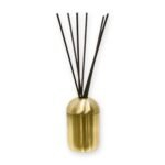 Slim metal reed diffuser vessel with dome lid and brushed gold finish holding seven dark reeds, on a white background